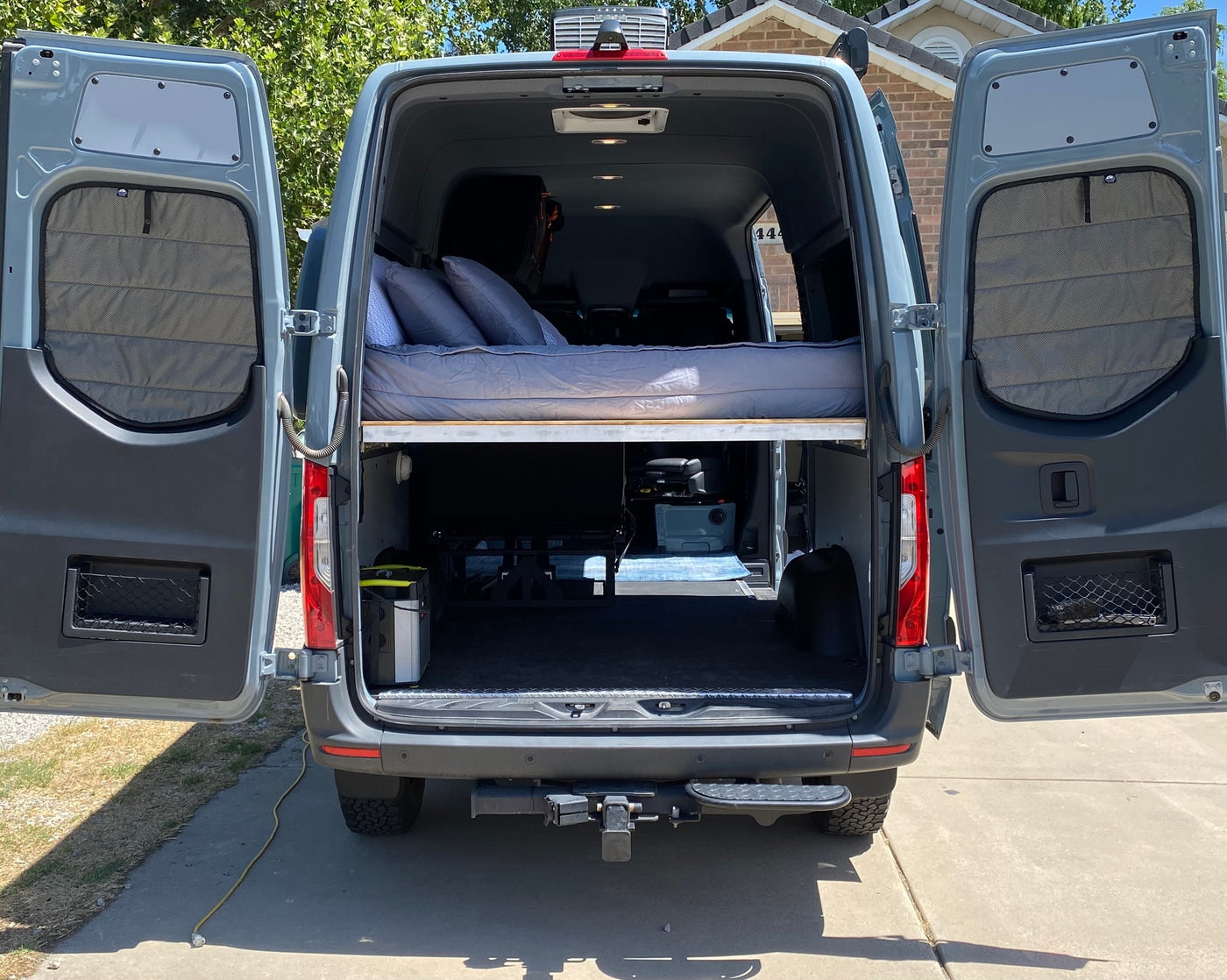 Grey camper van interior for RV rental, showing an elevated bed, under-bed storage, and open rear doors. — photo 19