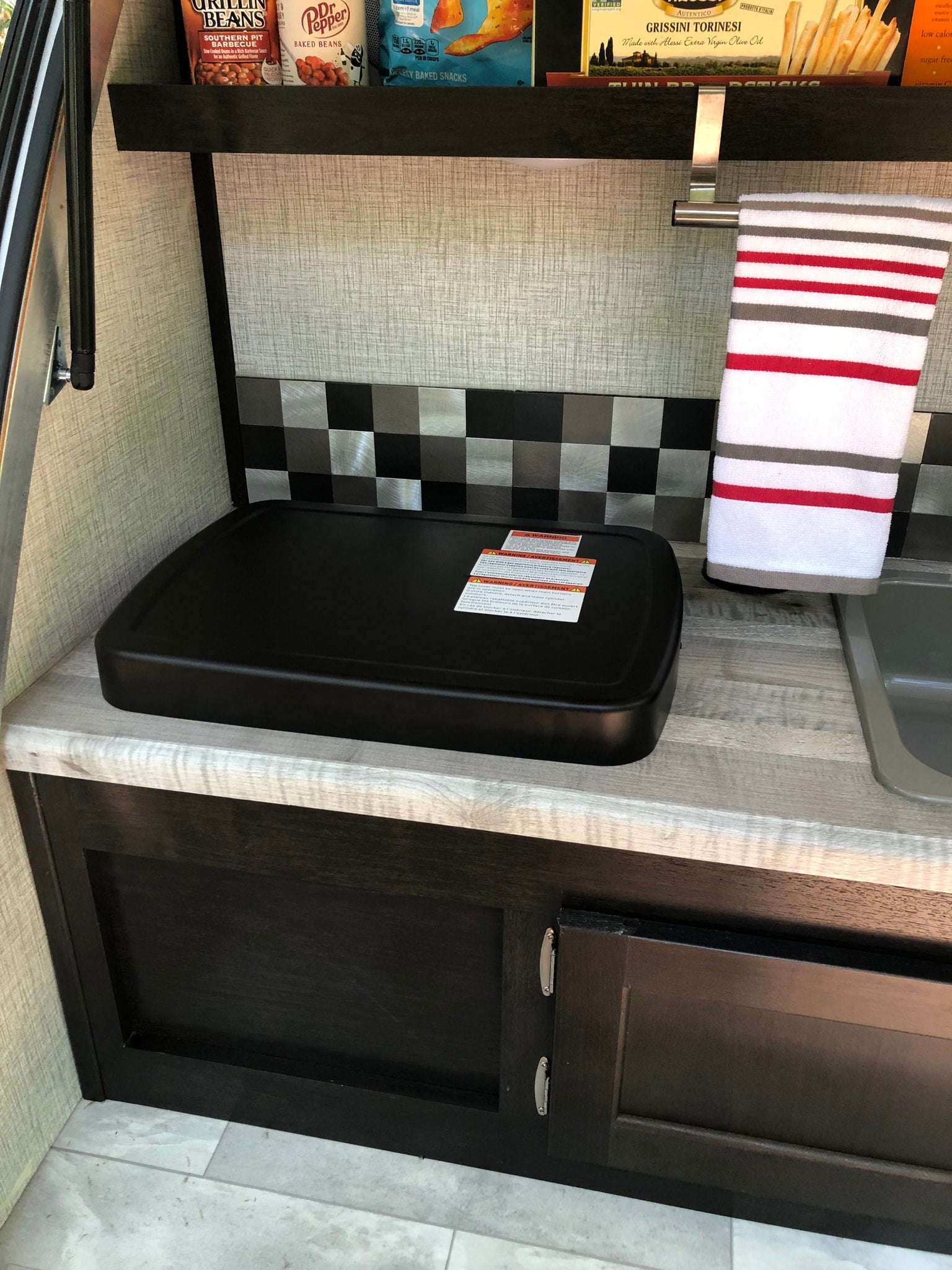 An RV rental's efficient kitchenette: griddle, sink, and a stocked shelf for travel cooking.