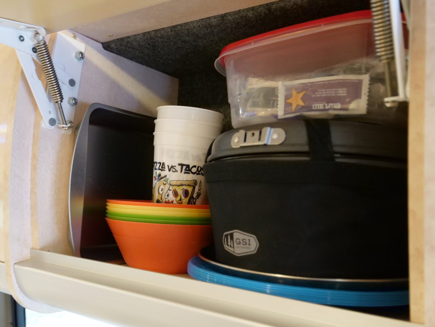 This rv rental cabinet holds kitchen essentials like stacked colorful bowls, cups, and a GSI Outdoors cooking set.