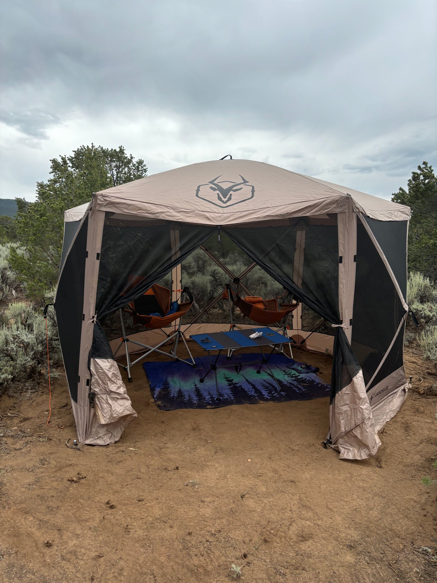 Enhance your RV rental camping with this comfortable portable screen house. Features chairs, table, & mat in nature.
