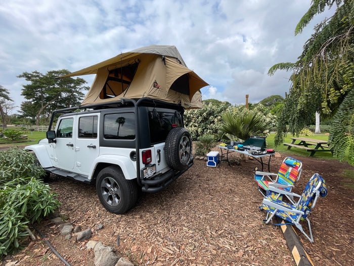 White Jeep Wrangler with a rooftop tent at a campsite, offering an RV rental alternative for comfortable outdoor adventures.