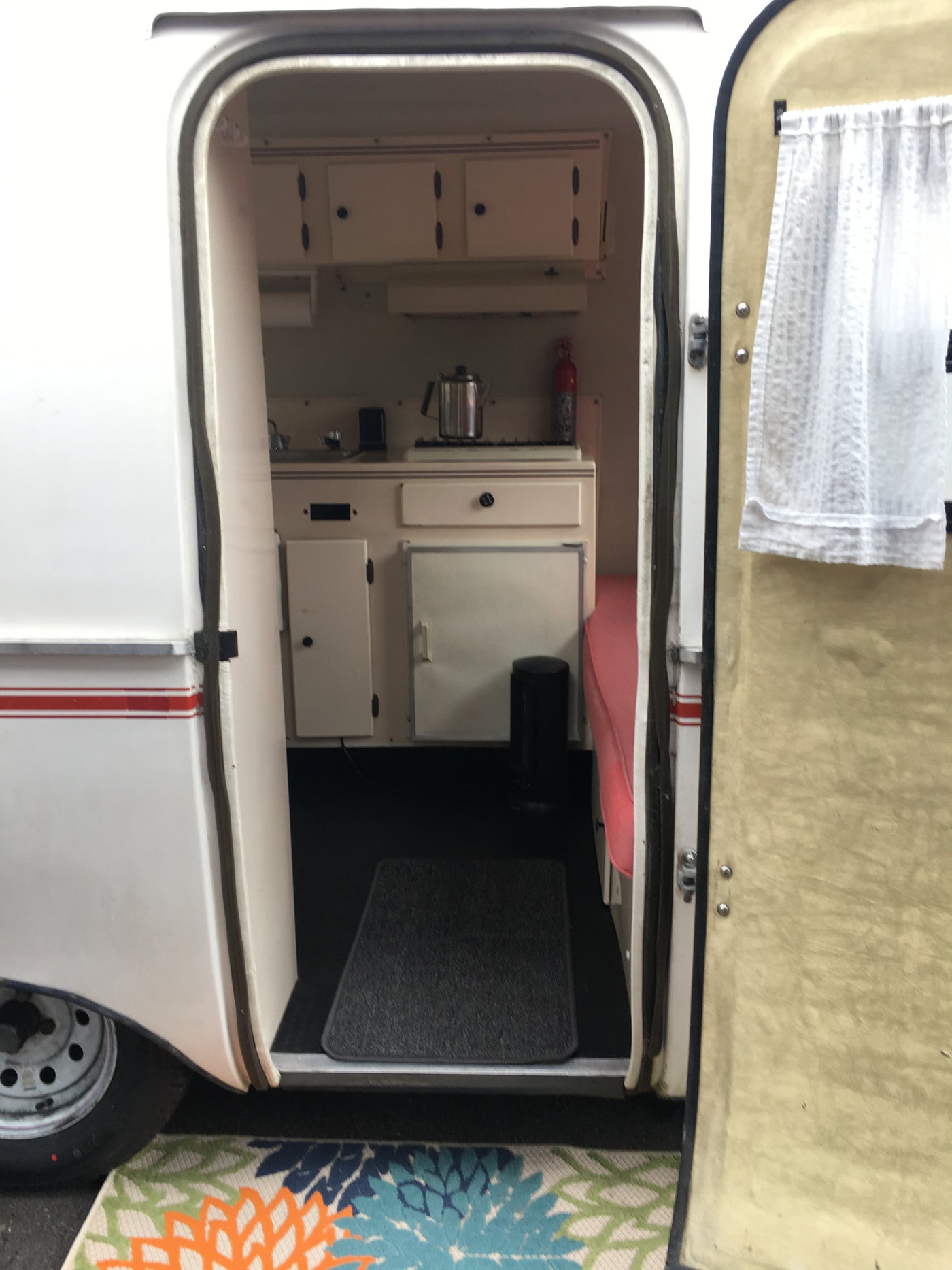 Open door view of a compact RV rental interior, showing a kitchen with sink/stove, cabinets, and a seating area. — photo 5
