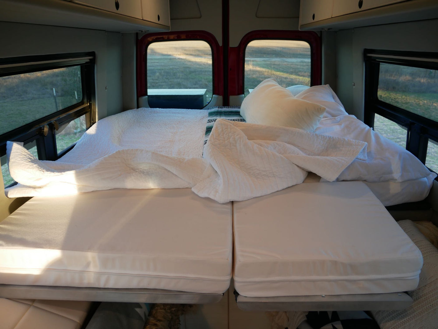 Inside a comfortable RV rental: a modular bed with white bedding, pillows, and scenic window views. Ideal for road trips.