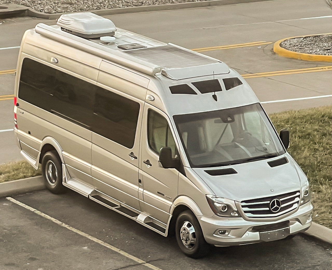 A silver Mercedes-Benz Sprinter RV rental parked outdoors, ready for travel adventures. Features solar panels and a rooftop AC unit.