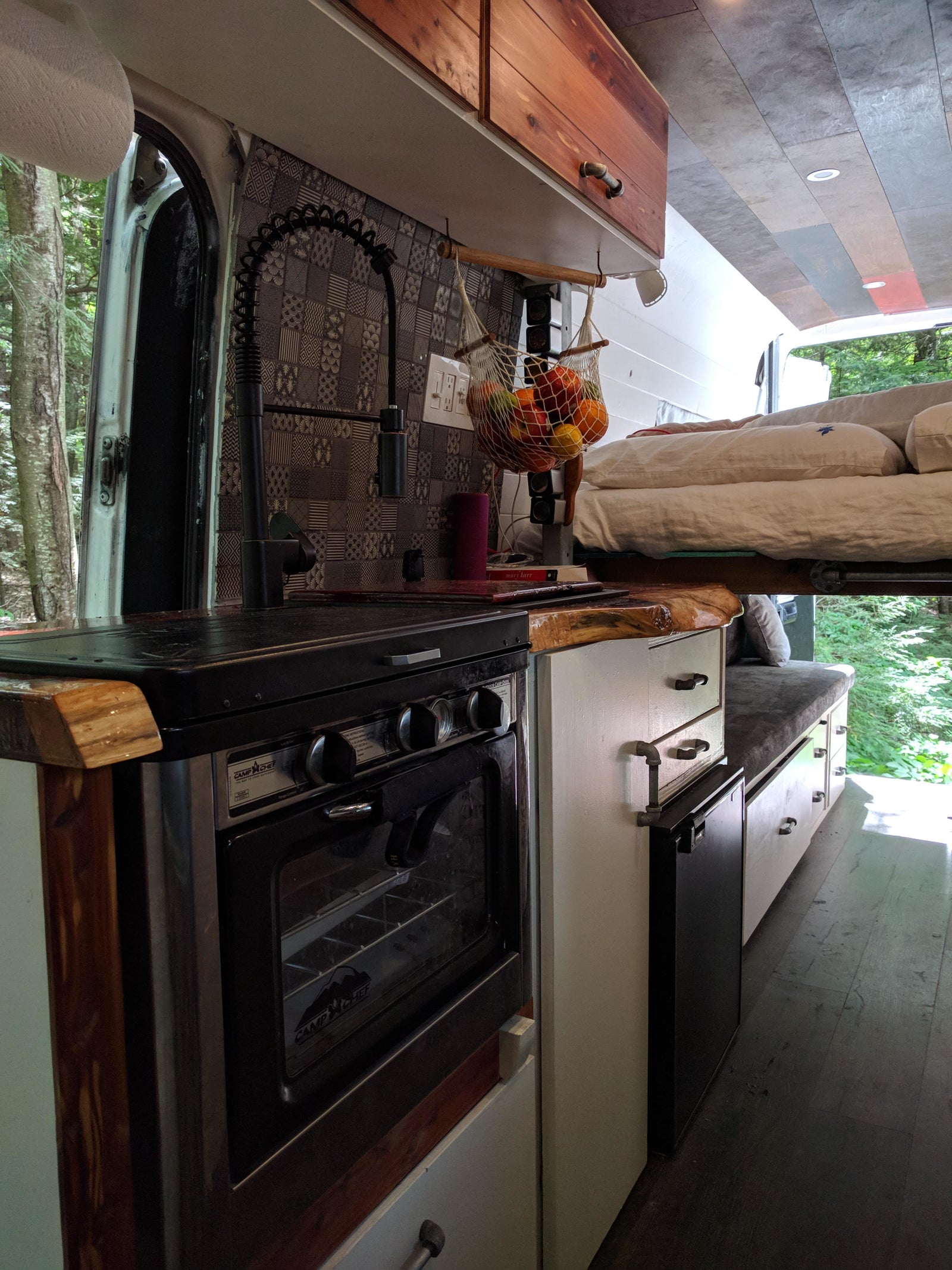 Cozy RV rental interior: Camper van with kitchen, bed, storage, and forest views through open doors.