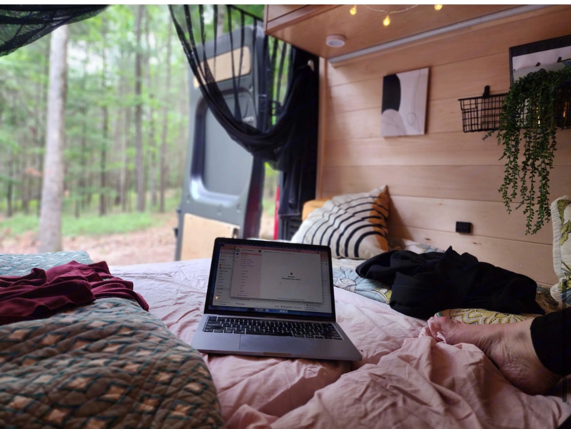 Working remotely from a comfy bed in an RV rental, with scenic forest views from the open doors.