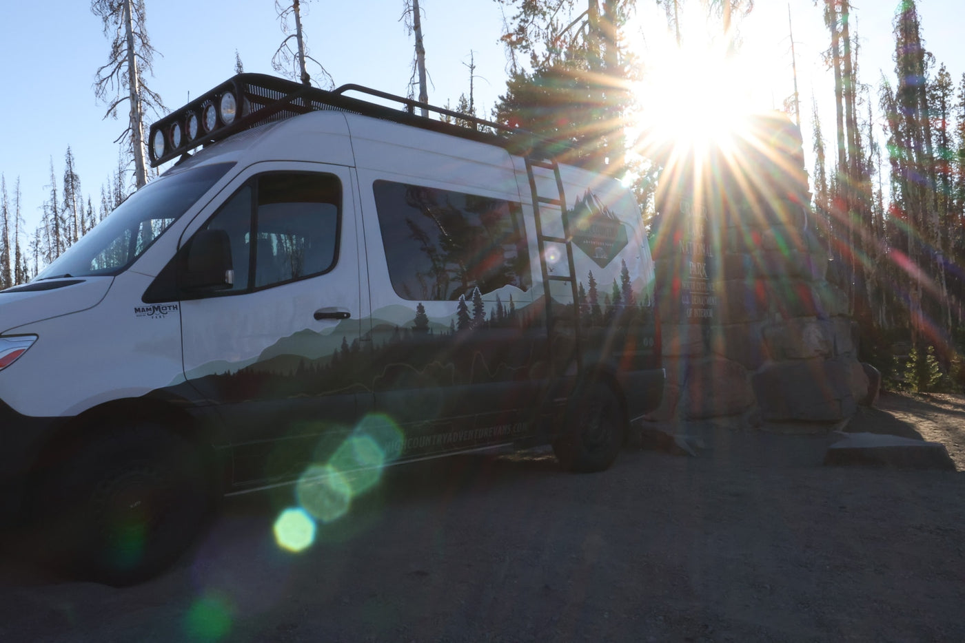 Bright sun illuminates a High Country RV rental van with mountain graphics at Crater Lake National Park entrance. — photo 9
