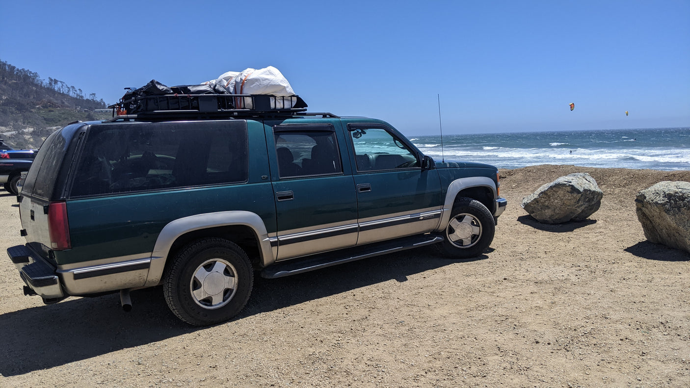 Green adventure SUV at the beach with kitesurfers. For road trips, an RV rental offers more space.
