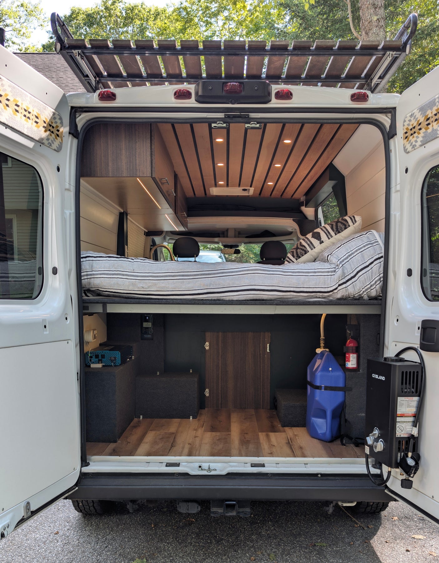 Inside a custom camper van, viewed from the back. Features a cozy bed, ample storage, and utilities, ideal for an rv rental.