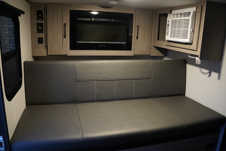 Compact RV rental interior featuring a comfy bench, built-in fireplace, and AC unit for comfortable travels.