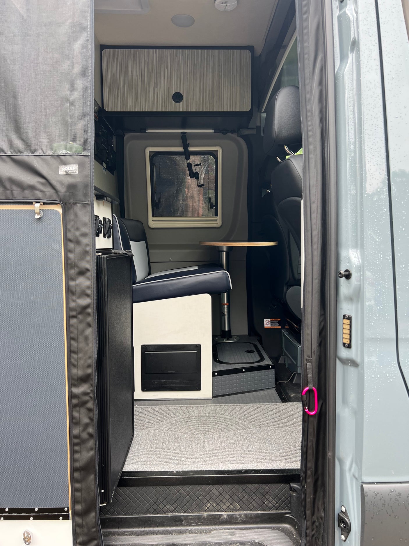 Interior of an RV rental: modern design with a comfortable dinette, window, and storage, seen from the open side door.