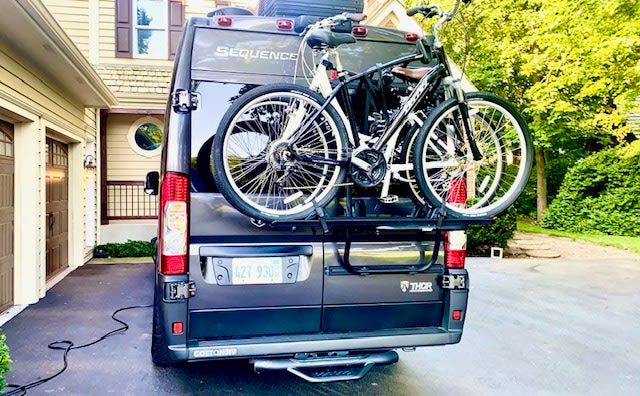 Dark grey Thor Sequence RV rental with bikes on its rear rack, parked on a driveway next to a house.