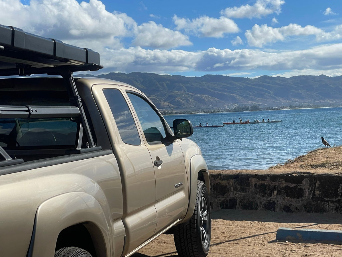Explore in a tan pickup with a roof-top tent by the ocean. Perfect RV rental for water adventures and mountain views.
