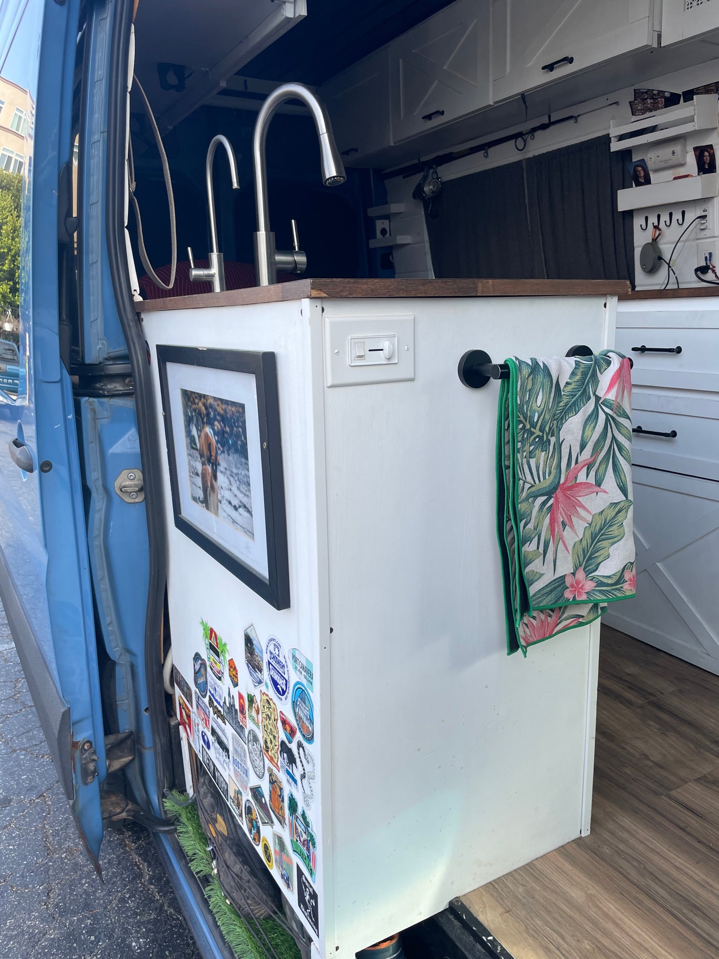 Compact RV rental interior featuring a kitchen with dual sinks, white cabinets, and a tropical towel, perfect for travel.