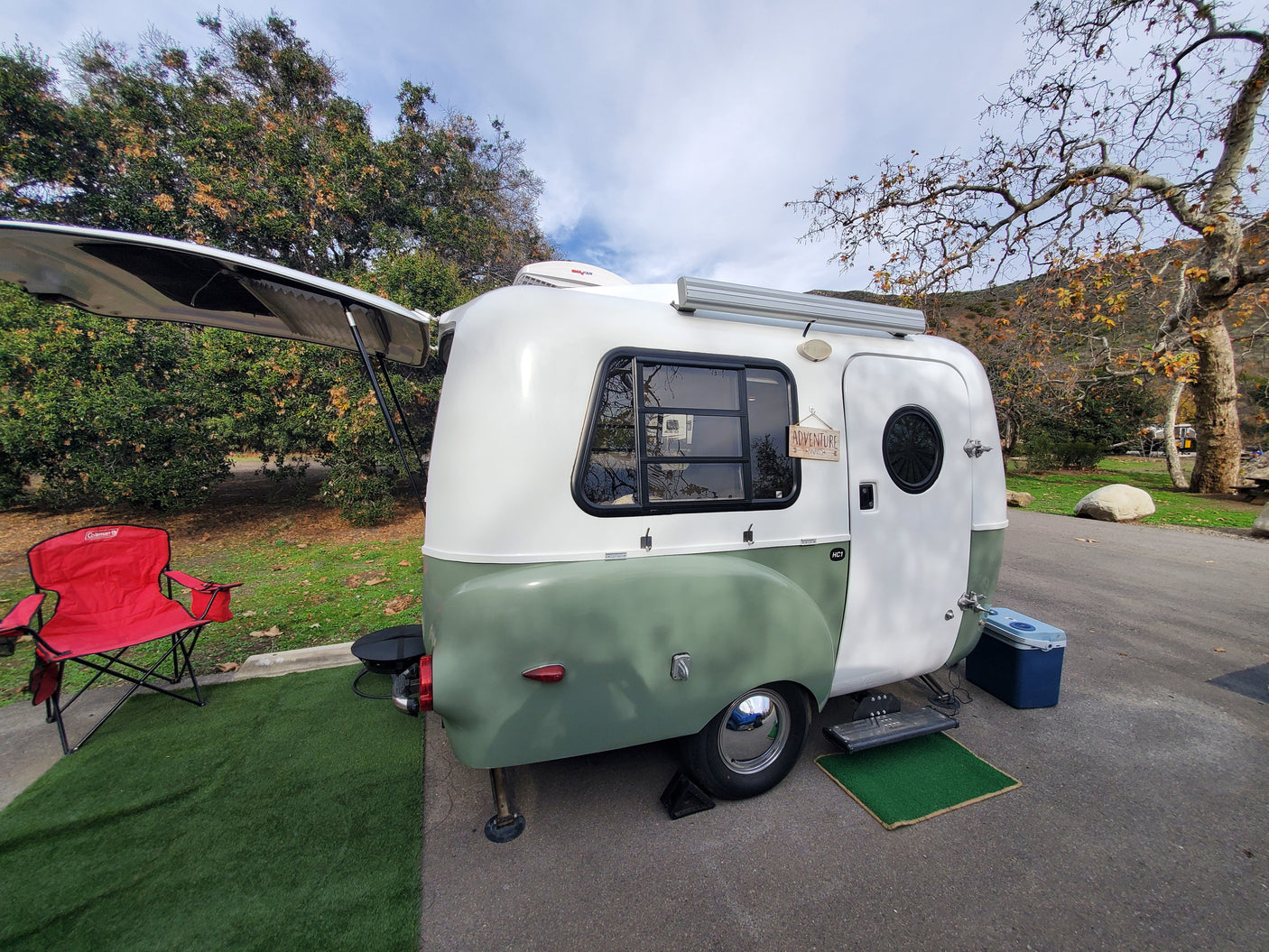 Charming retro-style camper, perfect for an rv rental adventure. Set up at a scenic campsite with a red chair.