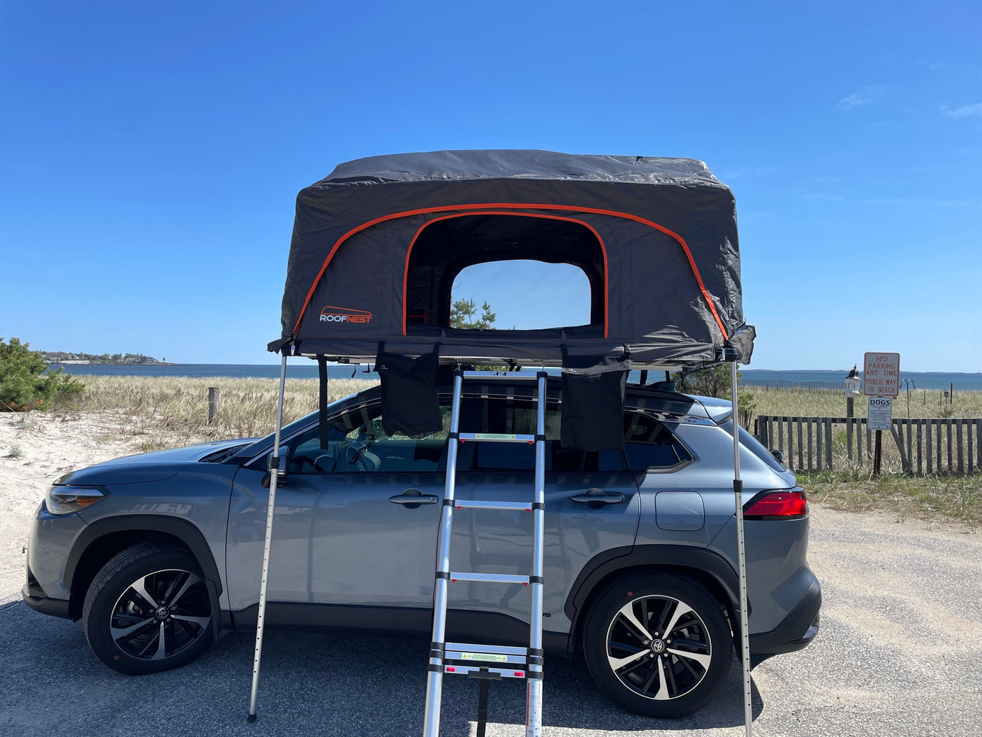 Grey SUV with deployed Roofnest rooftop tent. This car camping setup by the beach offers an alternative to an RV rental.