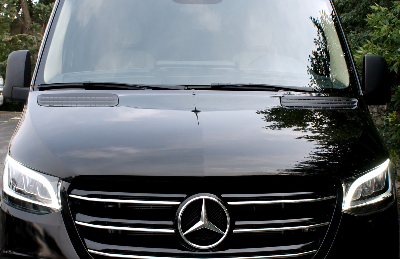 Up-close front view of a black Mercedes-Benz Sprinter van, highlighting its grille, logo, and LED headlights.