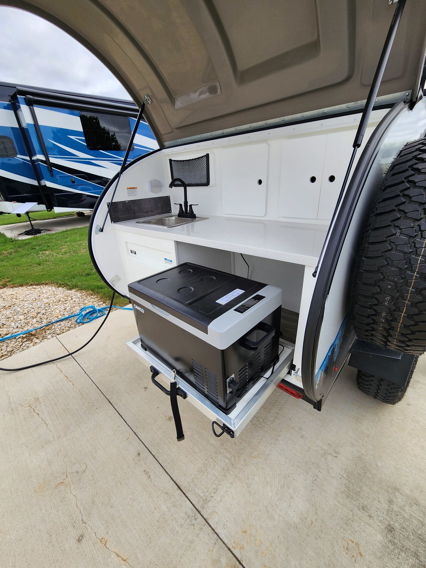 This rv rental teardrop camper's outdoor kitchen features a sink, faucet, and pull-out portable refrigerator.