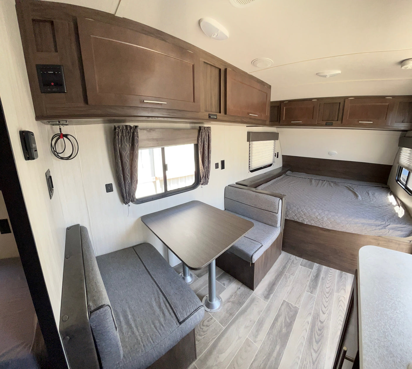 Spacious RV rental interior showcasing a cozy dinette, modern overhead cabinets, and a comfortable bed, perfect for travel.