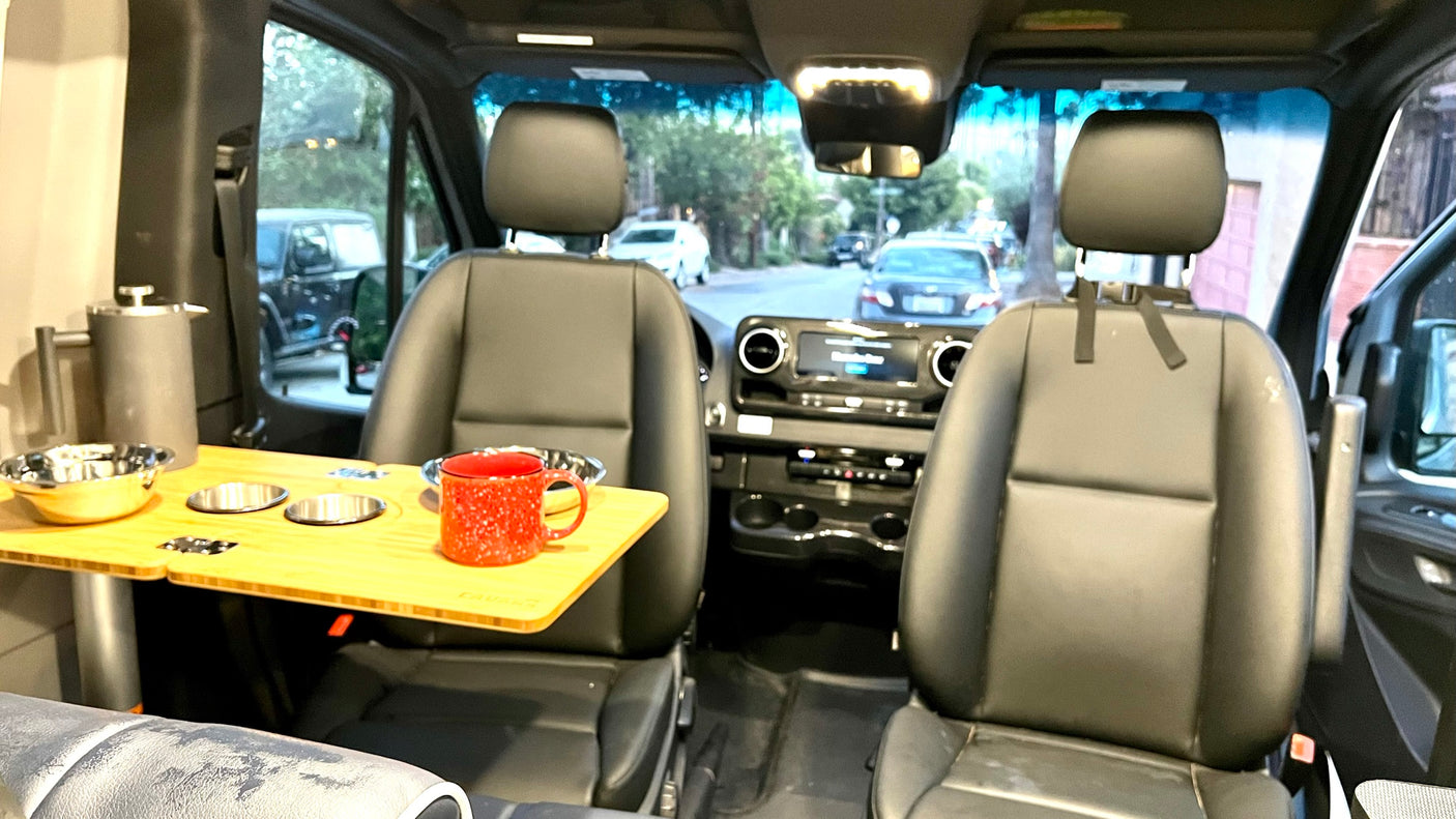 Cozy RV rental interior with swiveling front seats, a versatile table, and coffee setup. Perfect for camper van adventures.