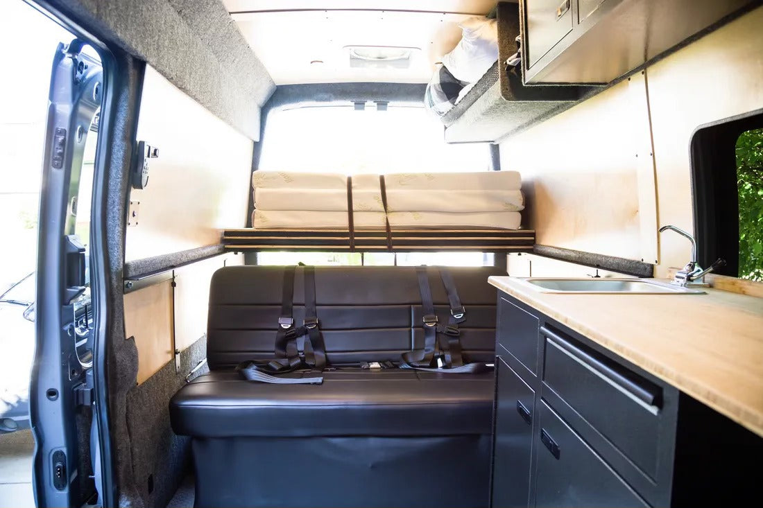 Inside a modern rv rental, featuring a versatile bench seat, an upper bed, and a compact kitchenette.