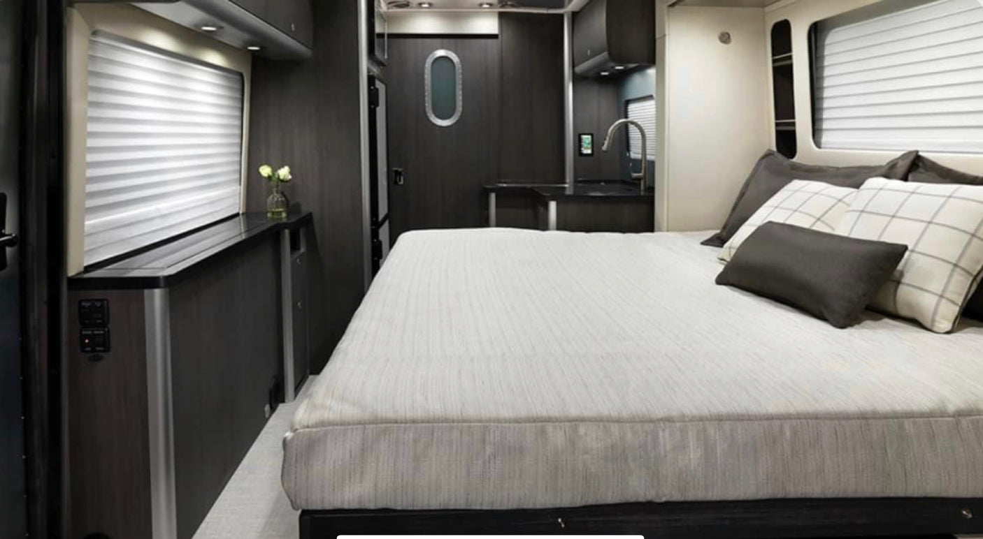 This RV rental features a modern interior with a comfortable bed, compact kitchen, and controls near the window for convenience.