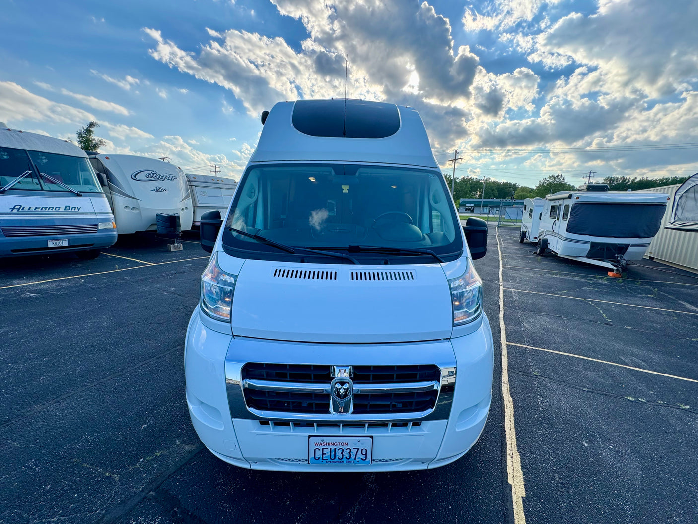 White RV rental van (WA plate CEU3379) in an RV parking area with other campers under a partly cloudy sky.
