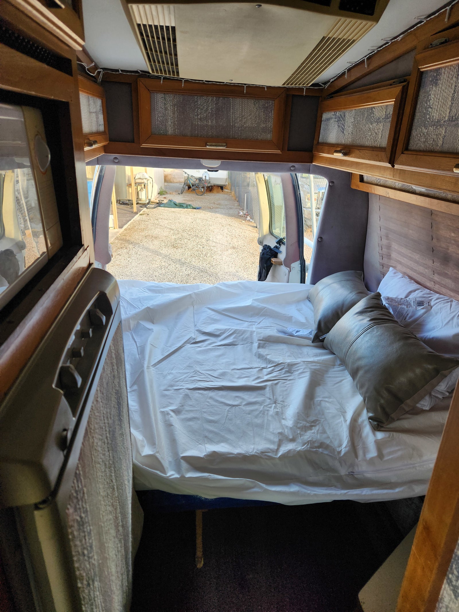 Cozy camper van interior, perfect for an rv rental, featuring a comfortable bed, overhead cabinets, and open rear doors to the outside.