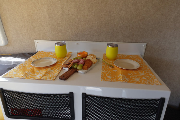 Cozy RV rental interior with a charcuterie board, plates, and yellow tumblers for a snack. Mesh storage nets are visible below.