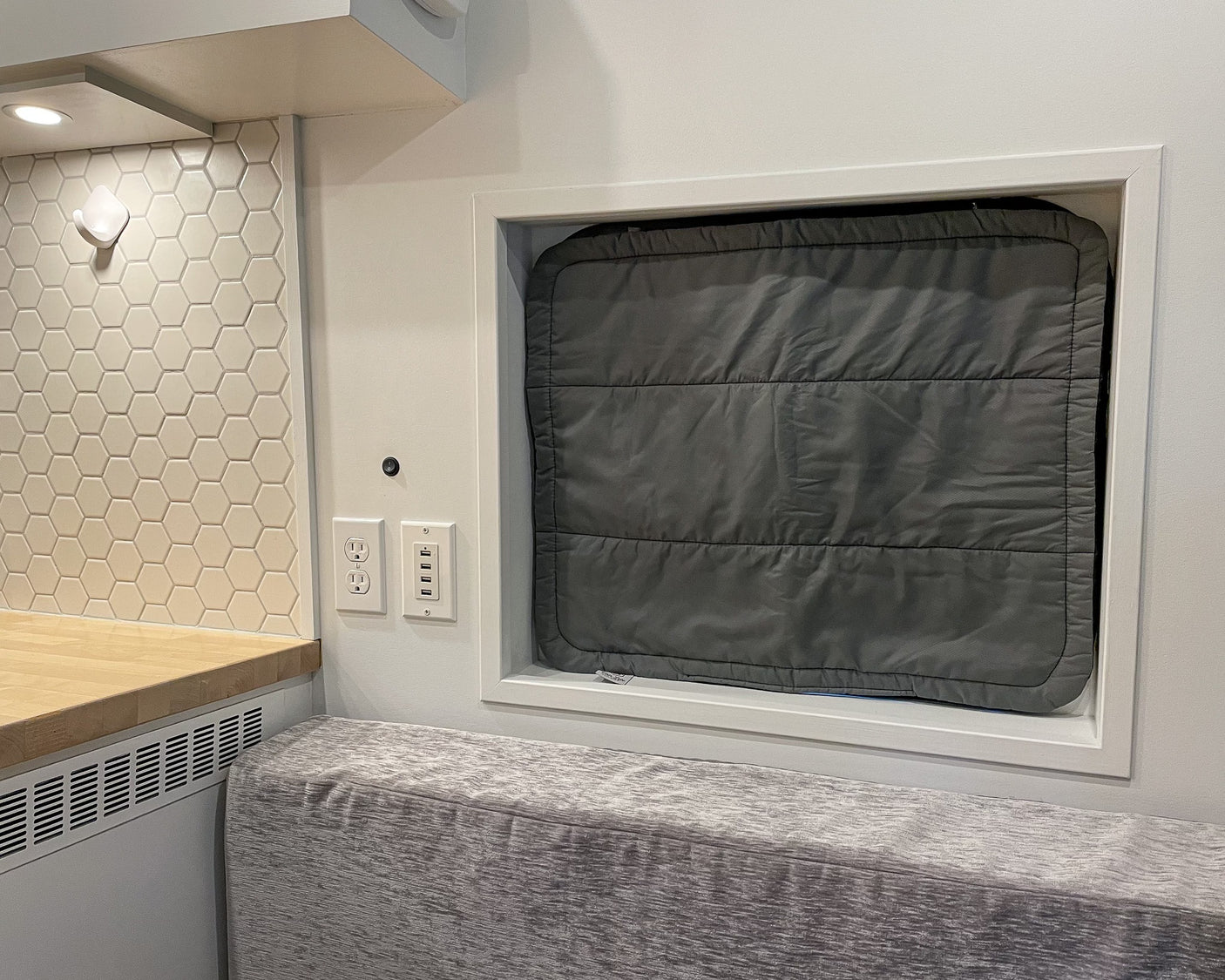 RV rental interior featuring a kitchenette with hexagon tile backsplash, USB outlets, and an insulated window cover over a cozy bench seat.