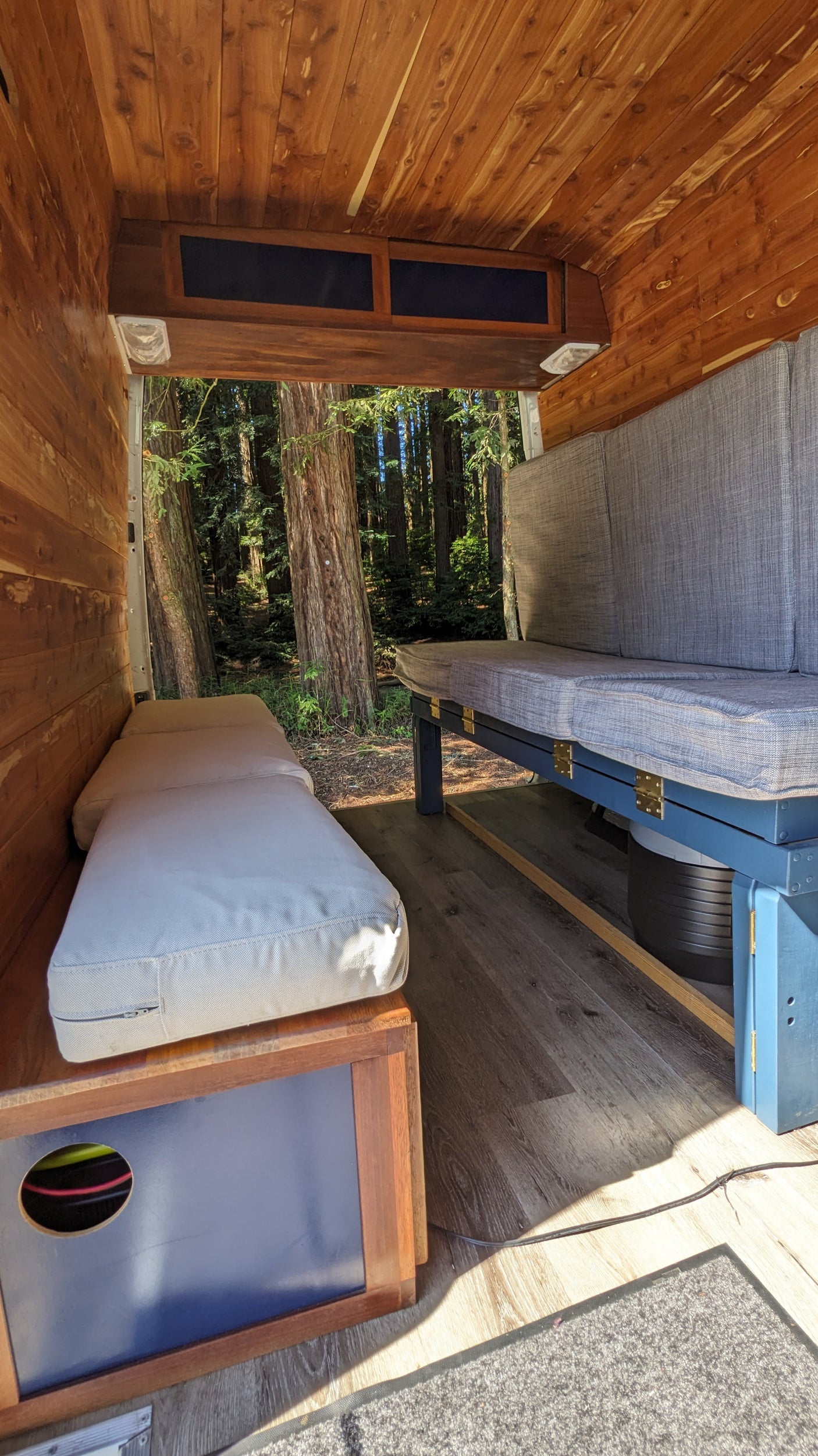 Cozy RV rental interior with warm wood paneling, comfortable seating, and an open view to a lush forest. Ideal for travel.