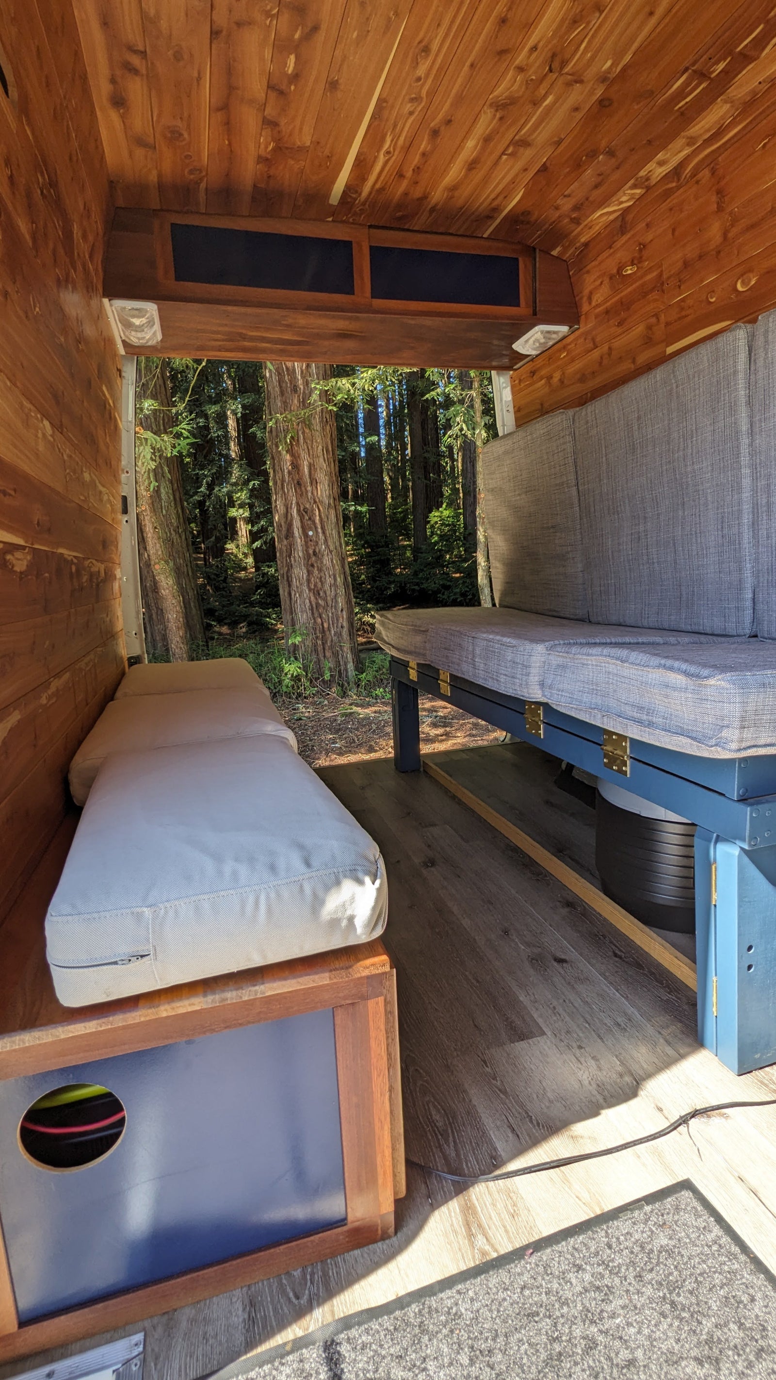 Cozy RV rental interior with warm wood paneling, comfortable seating, and an open view to a lush forest. Ideal for travel.