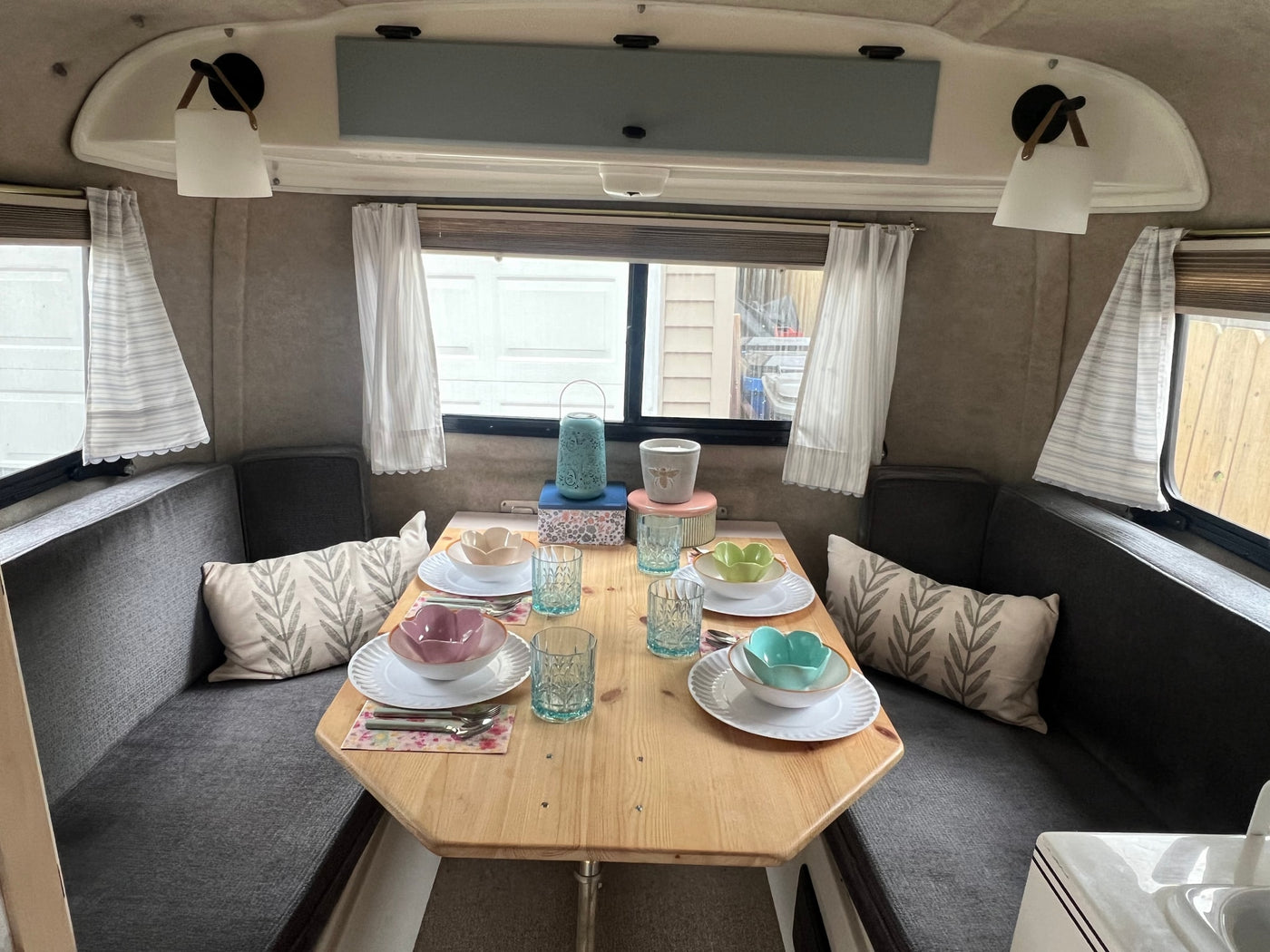 Cozy RV rental interior: A dining area with a wooden table, dark grey benches, and colorful place settings under soft lighting. — photo 6