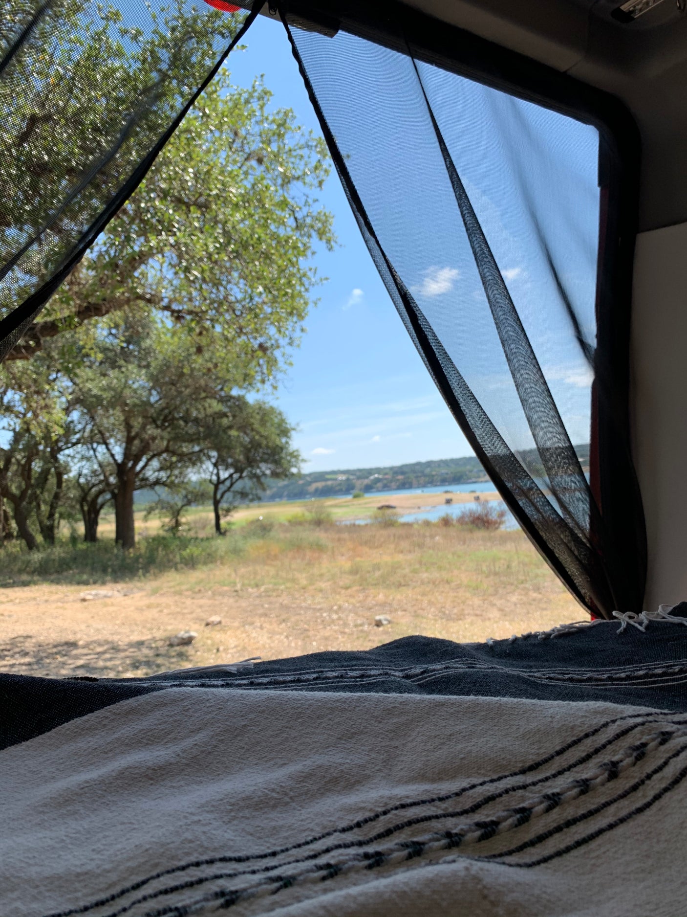 RV rental view: tranquil lake & trees seen from inside, with a screen & blanket.