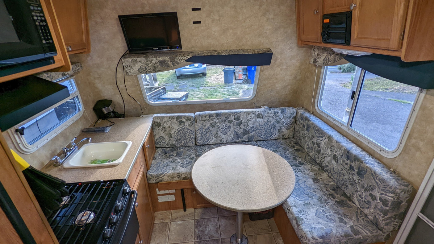 RV rental kitchen and dinette area, featuring a stove, sink, microwave, TV, and patterned cushions. Great for travel.