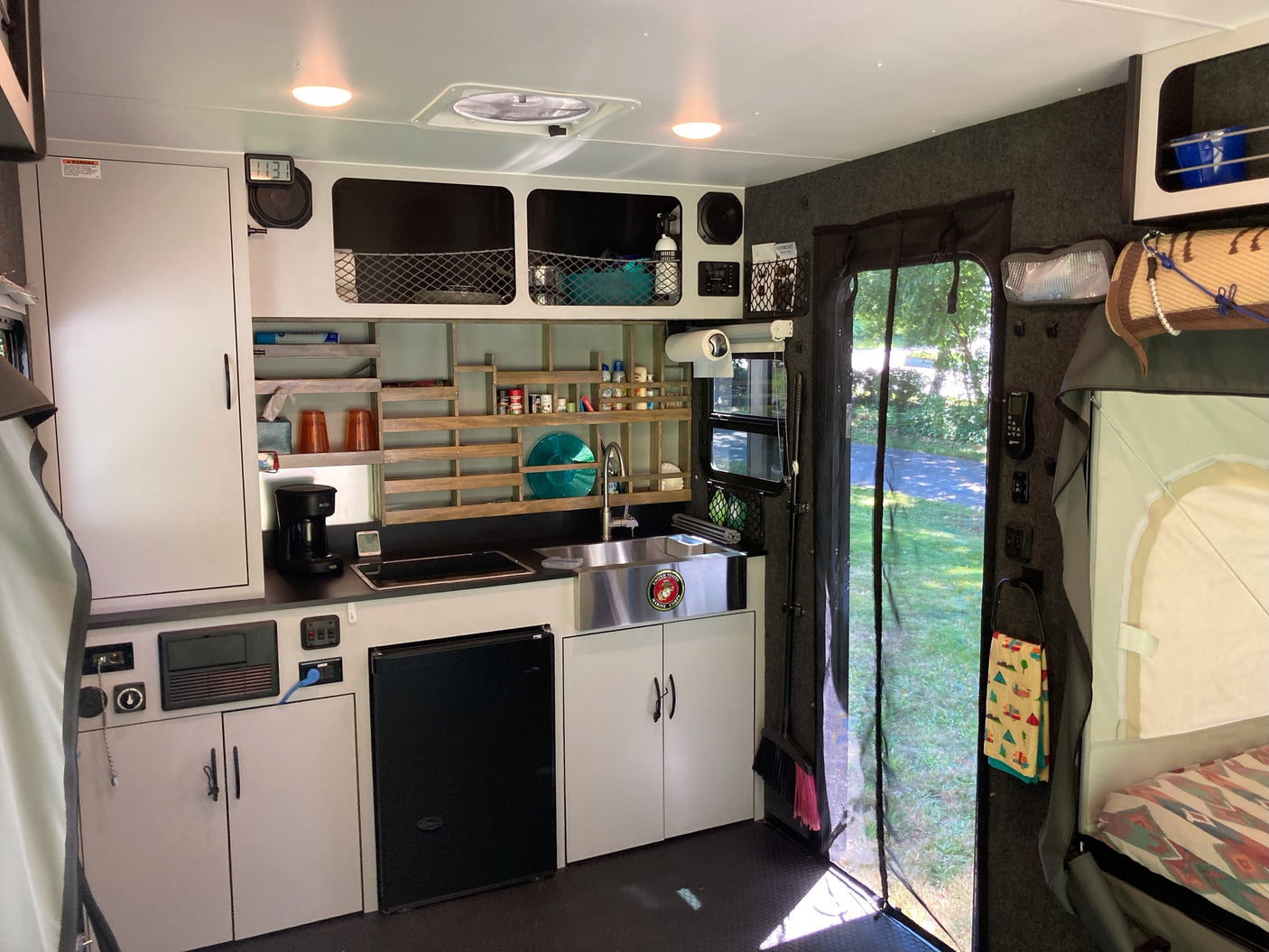 This RV rental interior features a compact kitchenette with a sink, stove, fridge, and clever storage, plus a cozy bed.