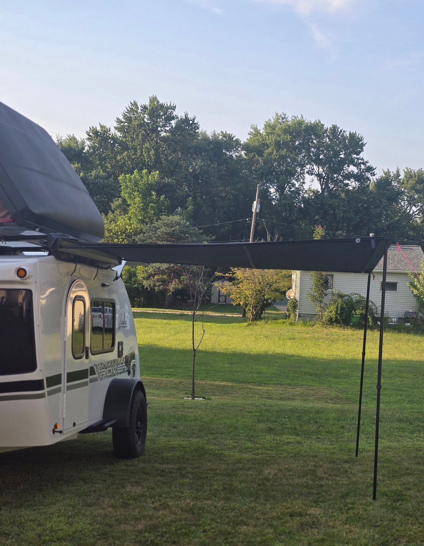 White teardrop RV rental with an extended black awning parked on a green lawn, ready for relaxing outdoor travel.