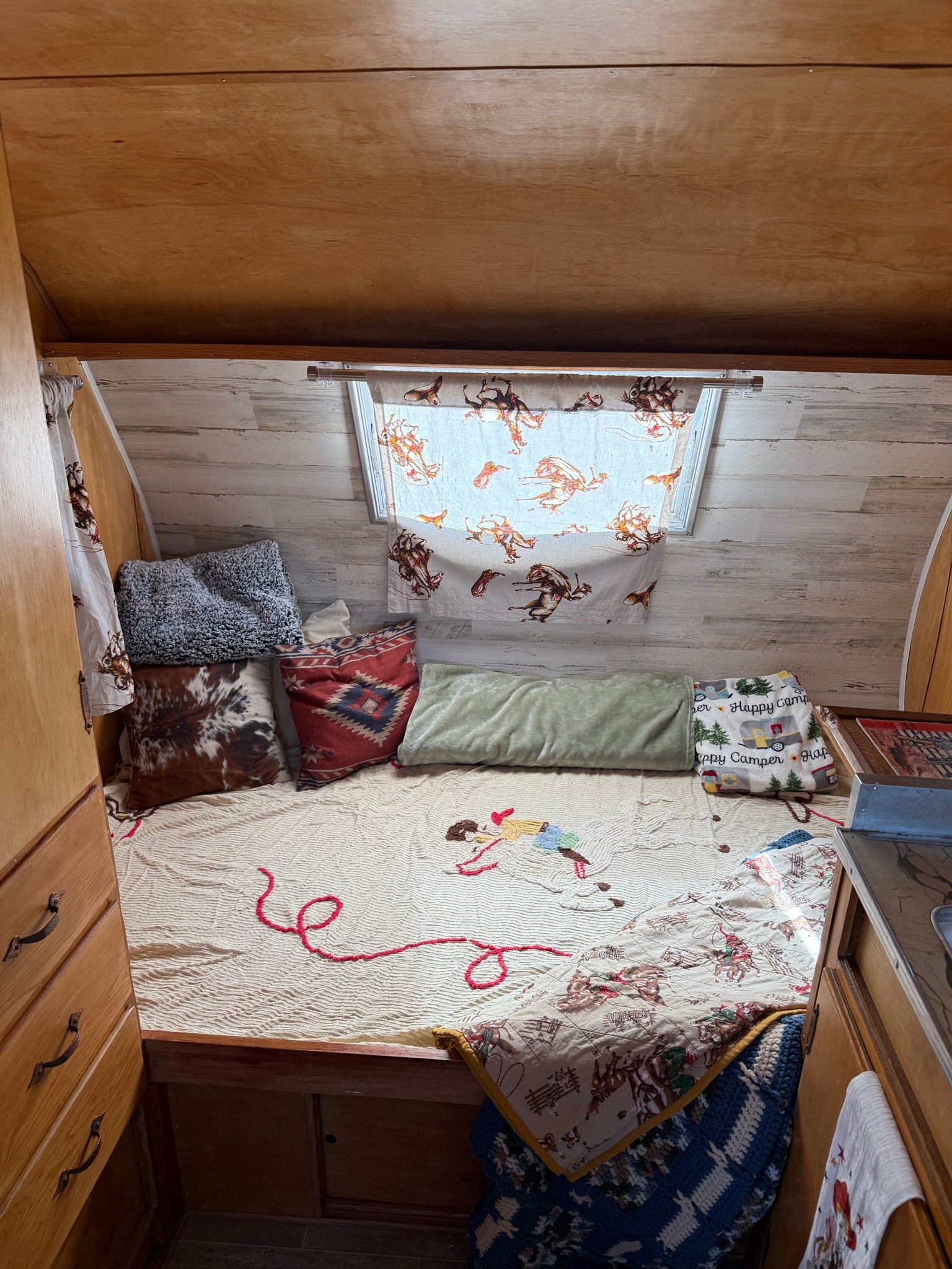 Cozy RV rental interior with western-themed bedding, a bed, and wooden cabinetry, creating a comfortable travel space.