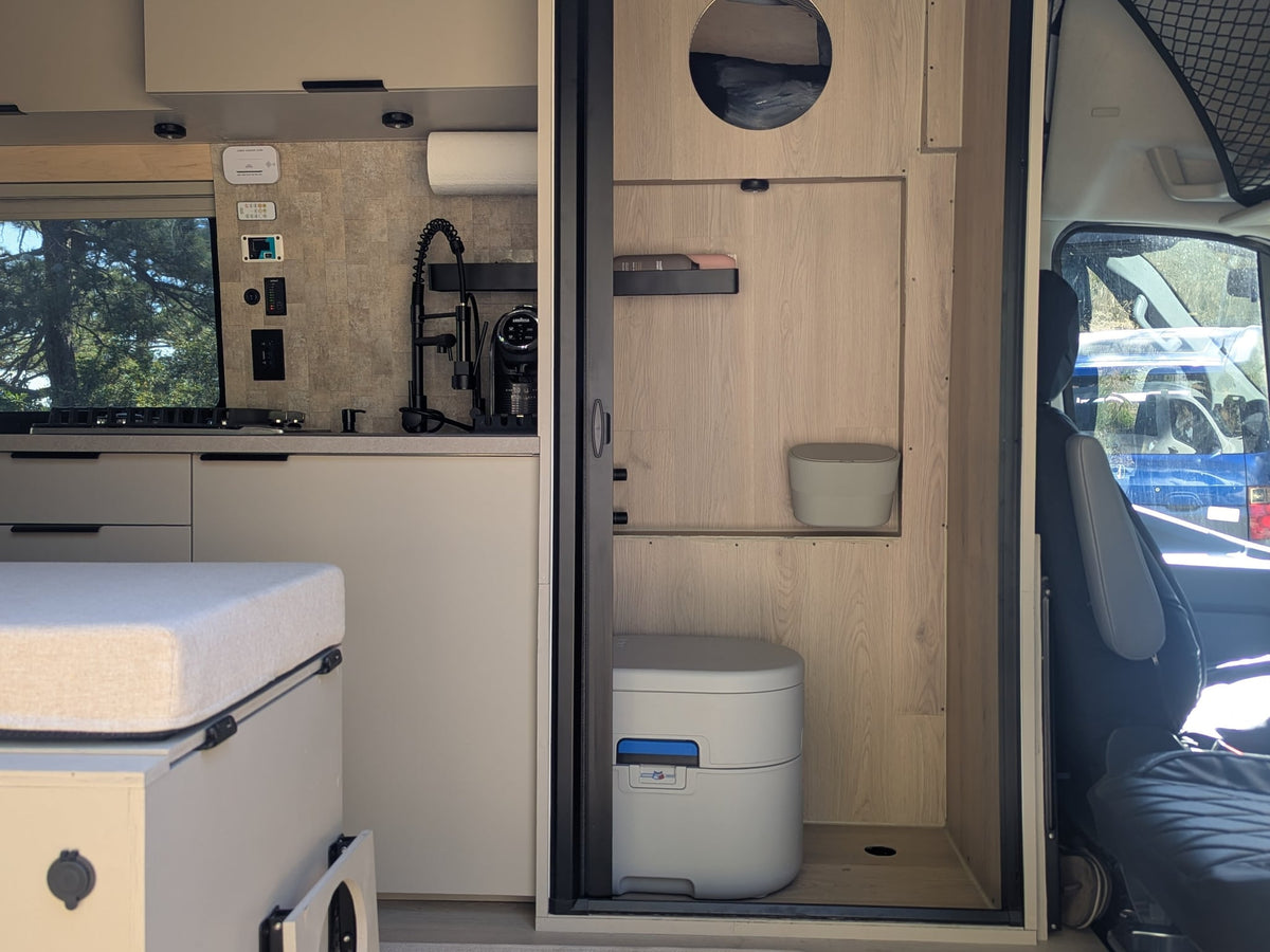 and a compact bathroom. Perfect for adventures.|An RV rental camper van parked at a scenic campsite with an open door — photo 3