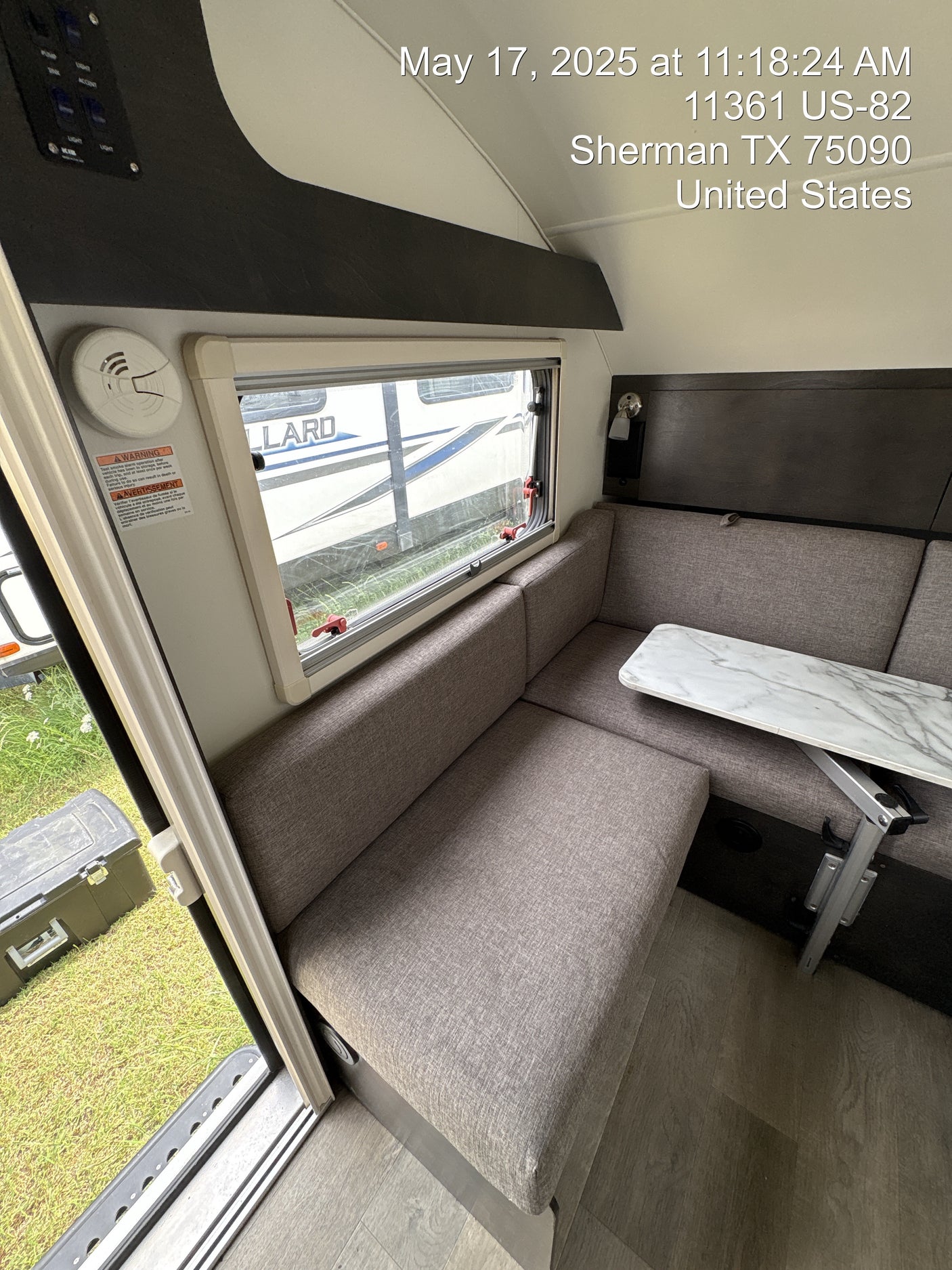 Compact RV rental interior: dinette with table & bench seating, window view, smoke alarm, and control panel.