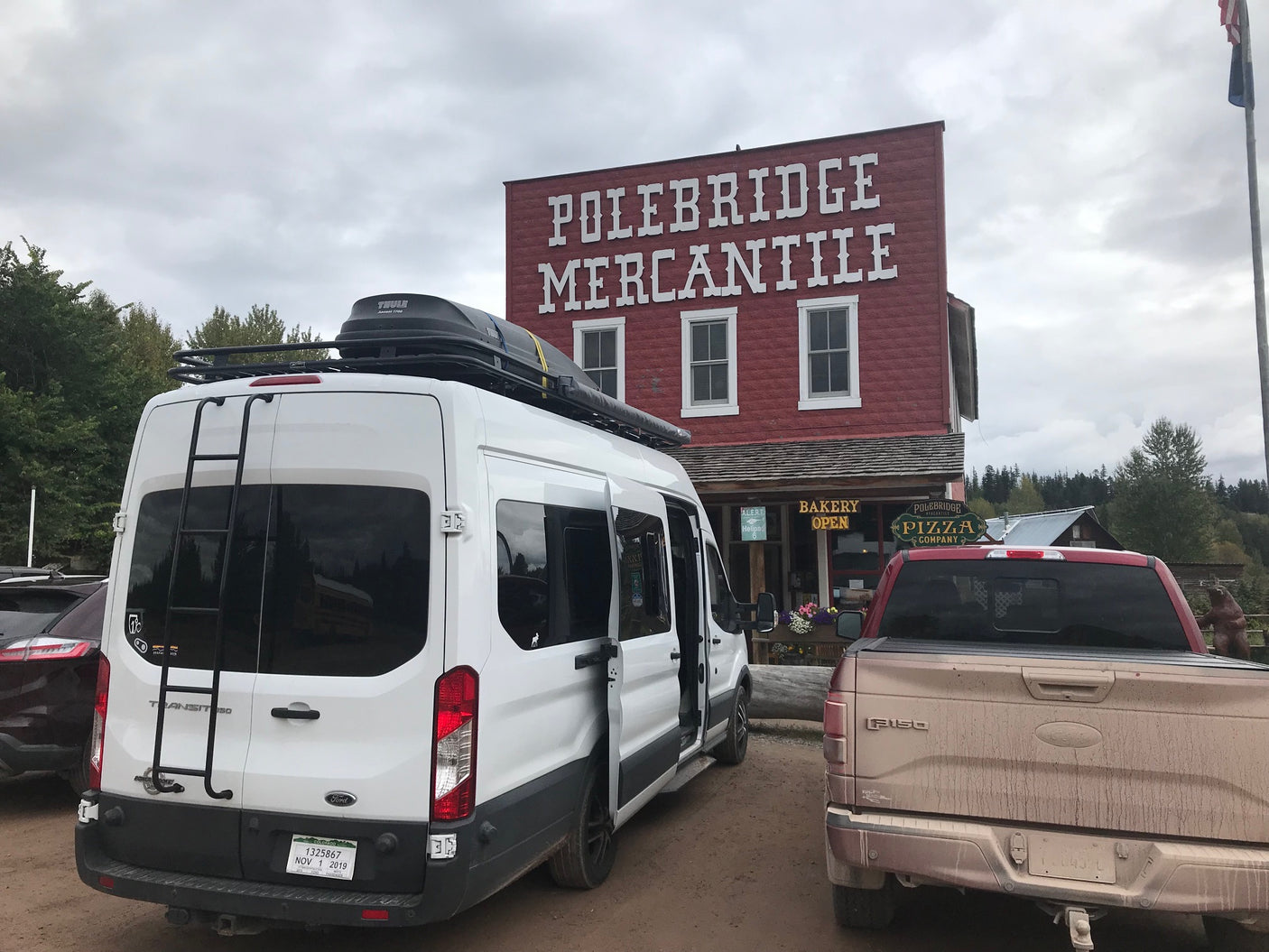 White Ford Transit RV rental parked at the rustic Polebridge Mercantile, a general store with bakery & pizza.