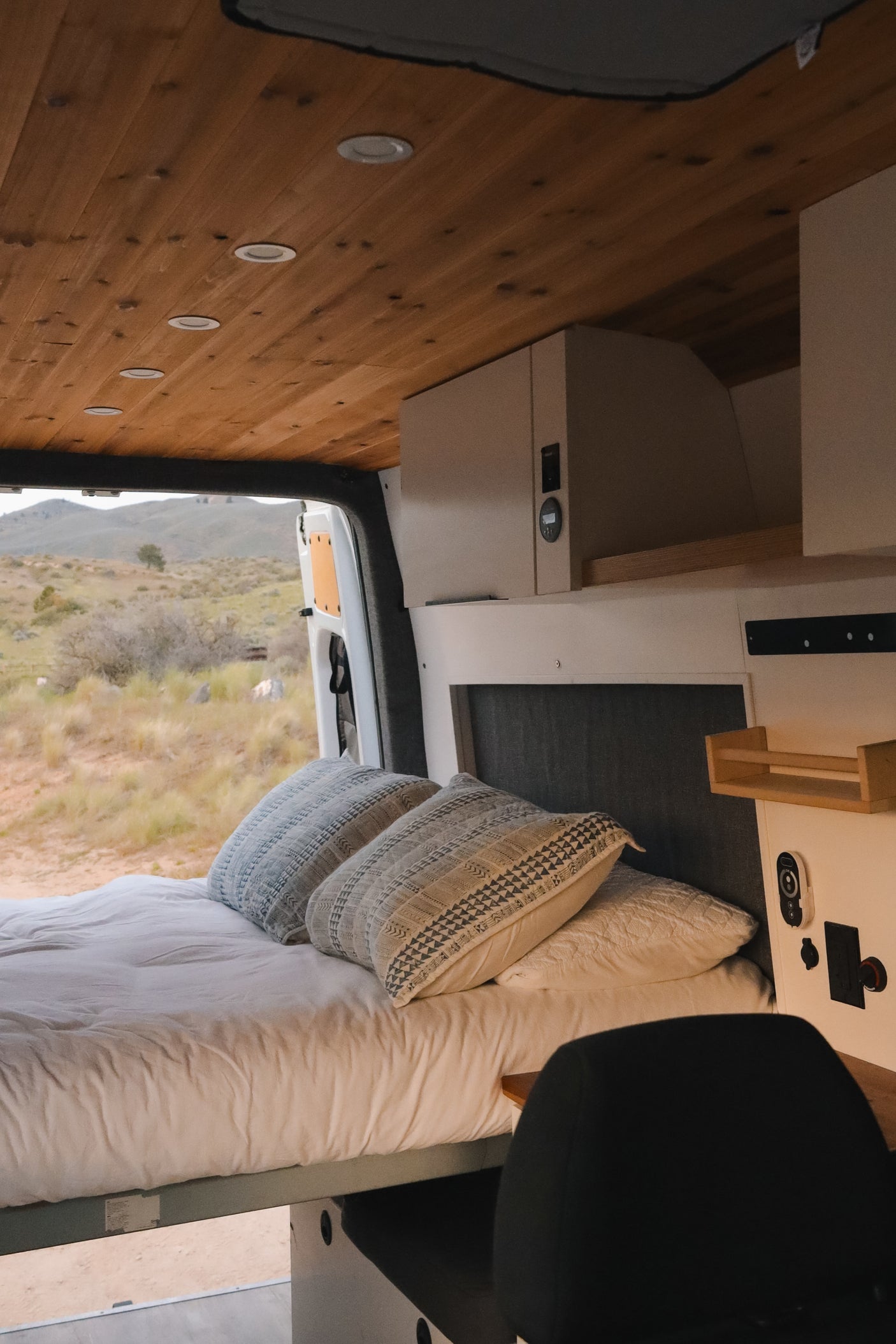 Cozy RV rental interior featuring a comfy bed, wood ceiling, and scenic desert views for a perfect van life adventure.