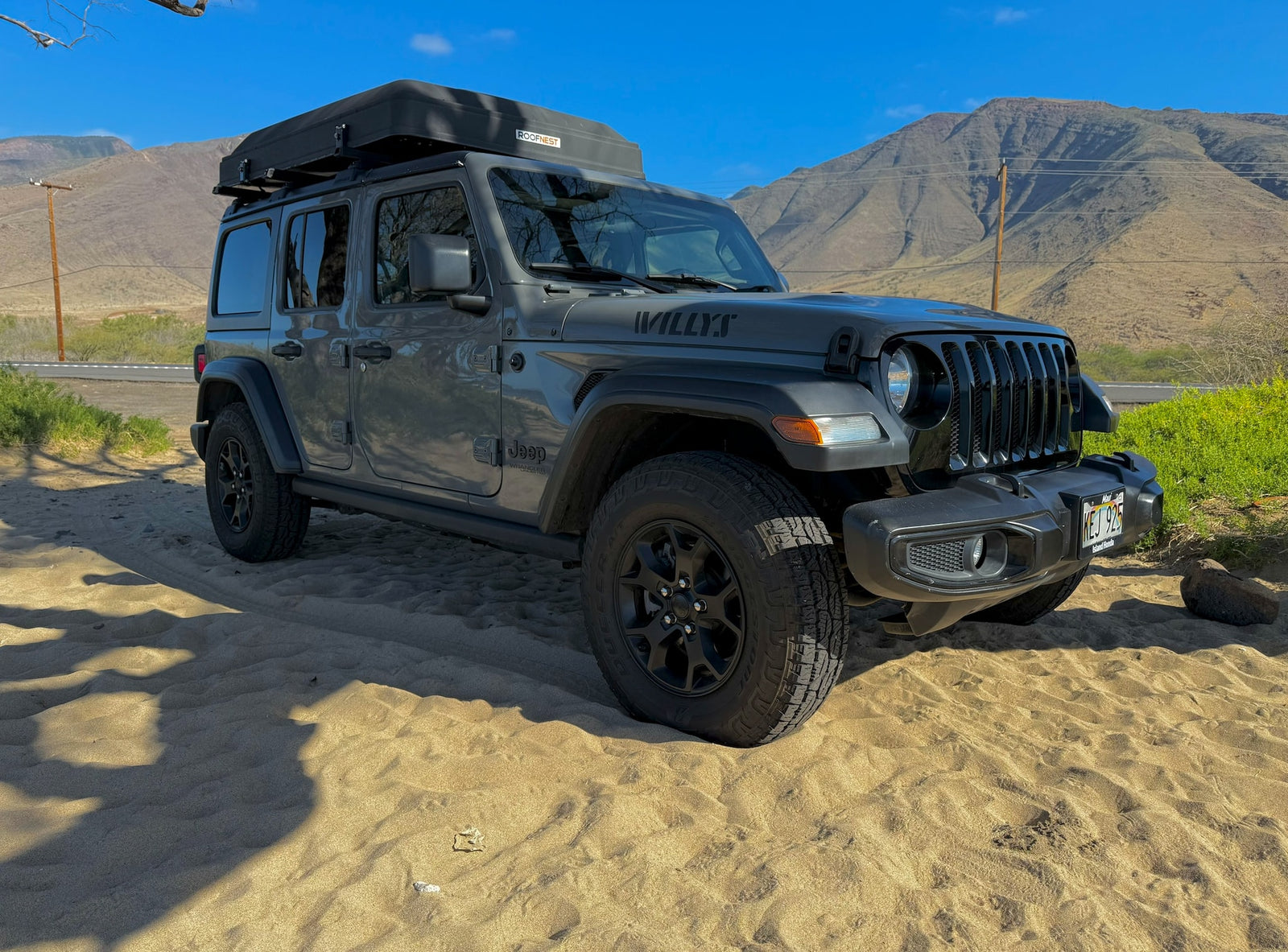 Gray Jeep Wrangler RV rental with rooftop tent on a Maui beach, mountains in background. Ready for island exploration.