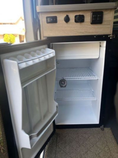 An RV rental's compact interior kitchen area, featuring an open mini-fridge and convenient power outlets.