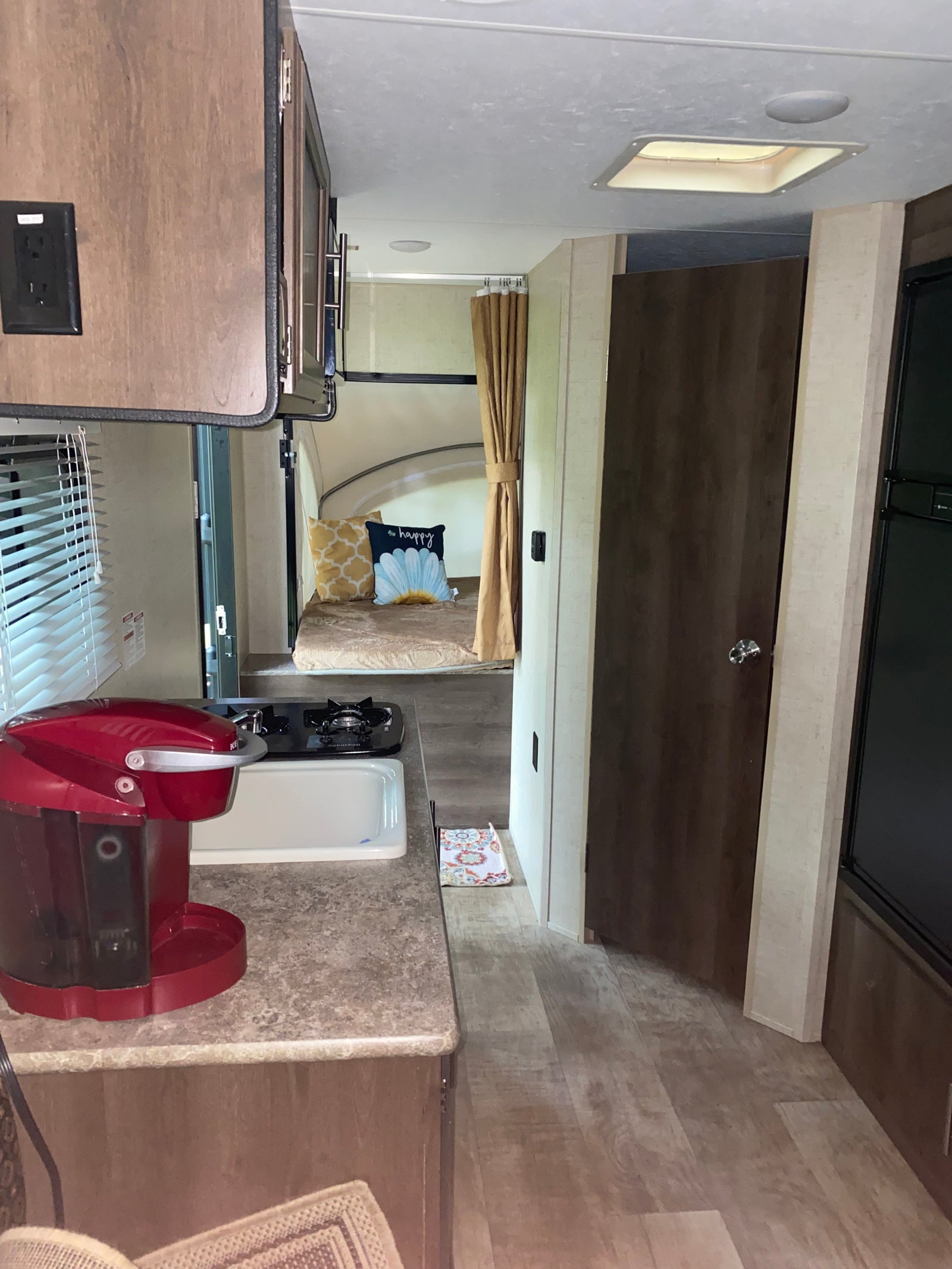 Inside an RV rental: a compact kitchen with sink, stovetop, and red coffee maker, leading to bunk beds in the back.