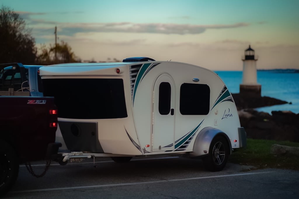 accented with teal stripes and blue underglow at dusk.|A white Luna teardrop camper