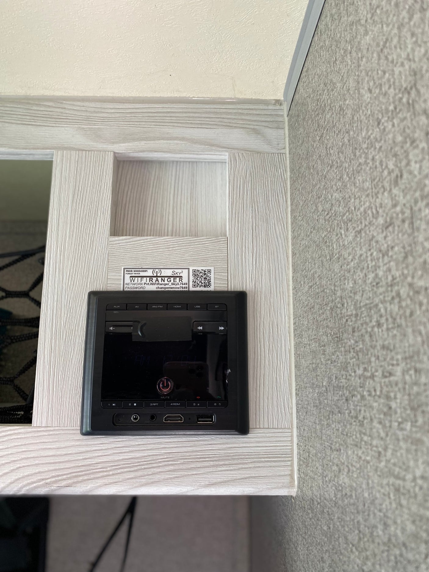Inside an RV rental: a black entertainment control panel, with Wi-Fi network and password visible on a label above it.