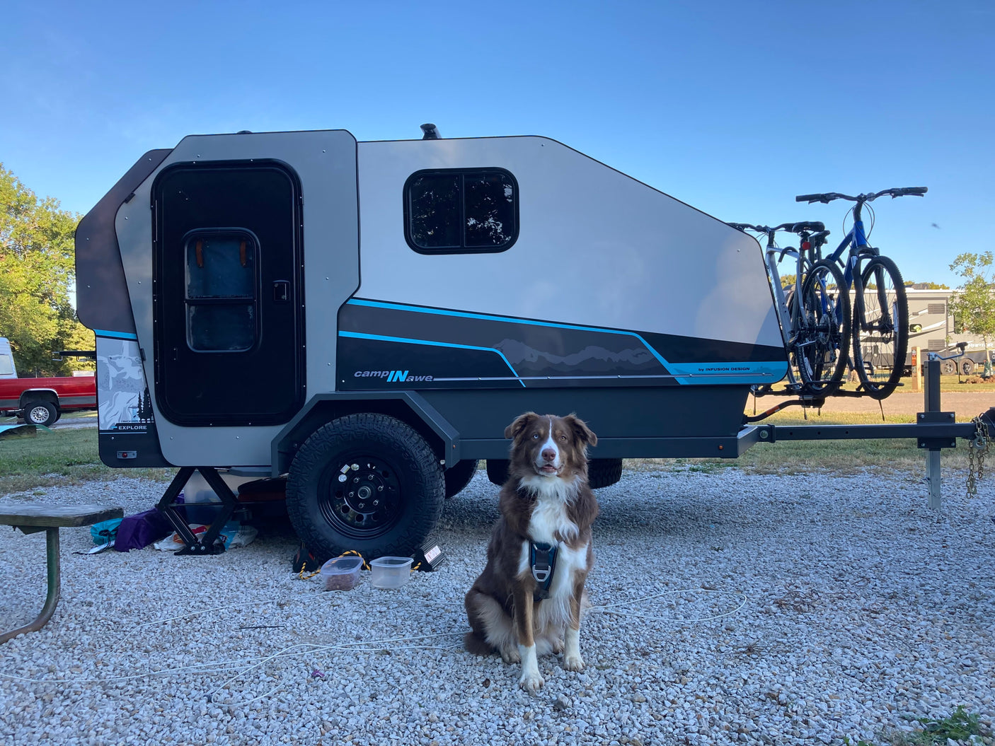 Your next rv rental adventure: A dog with a CampINawe teardrop camper & bikes at a gravel campsite.