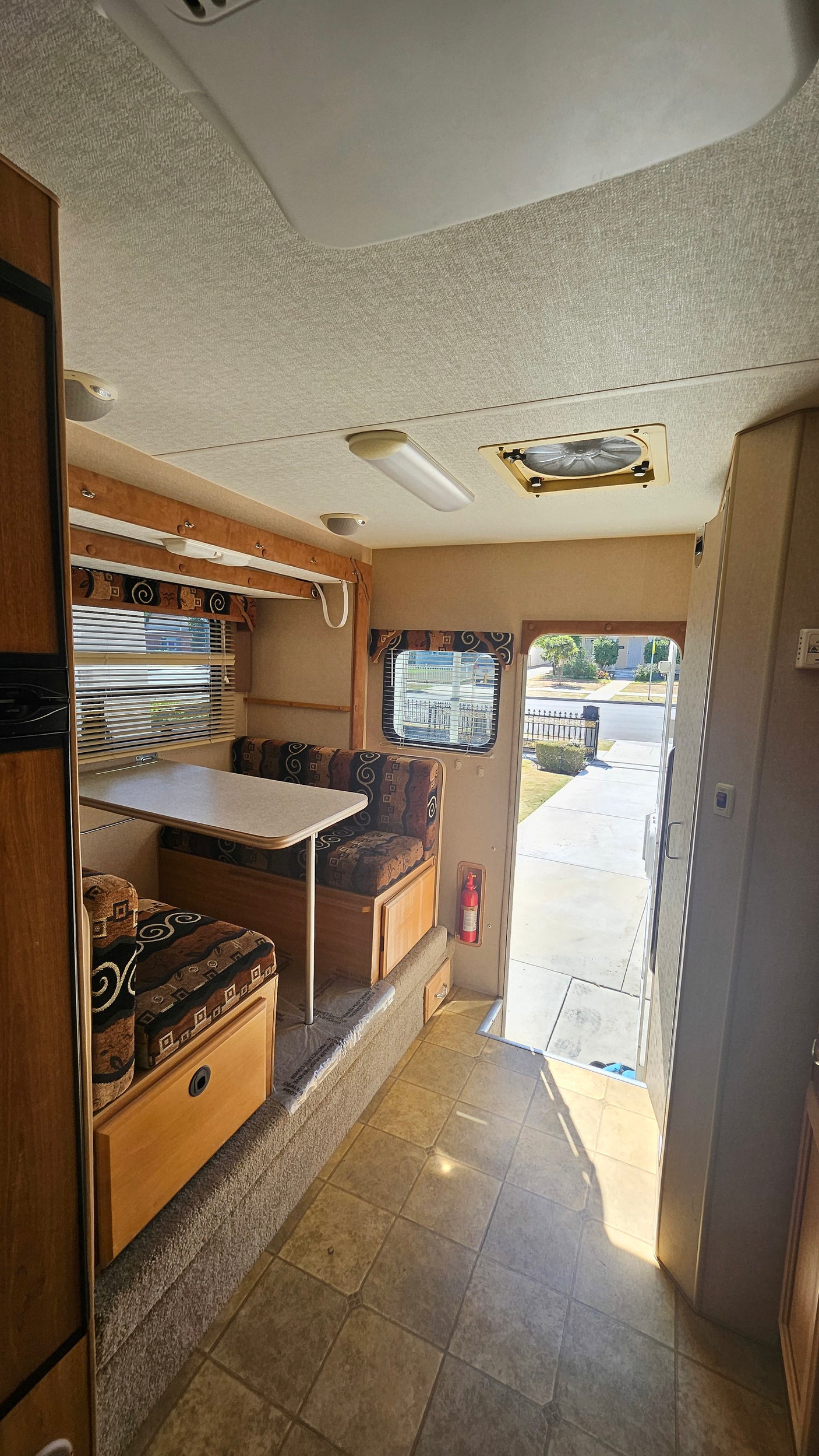 RV rental interior: dinette with patterned cushions, wood accents, tiled floor, and a view of the street outside.
