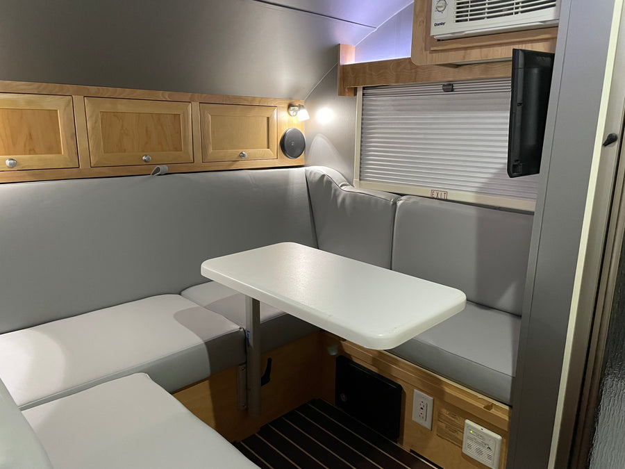 Cozy RV rental dinette area featuring U-shaped seating, table, overhead cabinets, TV, and AC unit.